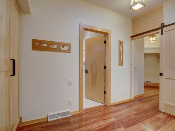 Sunny interior room with open wooden doors, hardwood floors, wall decor, and ceiling lights.