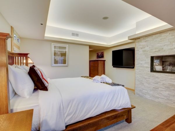 A neatly made hotel bedroom with a large bed, pillows and blanket, plus a mounted TV and a stone fireplace.