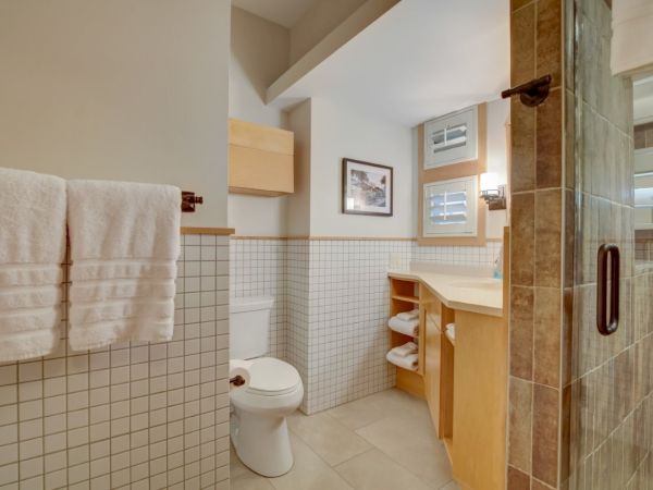 Bright tiled bathroom with toilet, vanity, folded towels, and a glass-door shower with rail.
