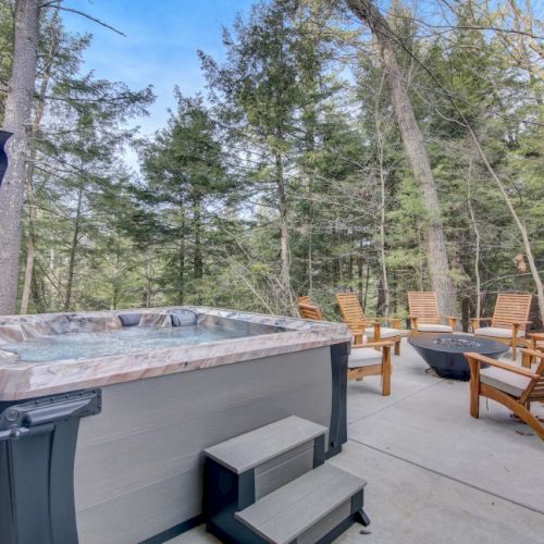 Outdoor patio with a hot tub and wooden lounge chairs among tall trees on a sunny day.