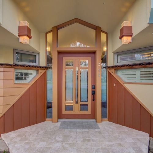 A modern home entryway with a red door, tiled porch, and side windows under a beige overhang.