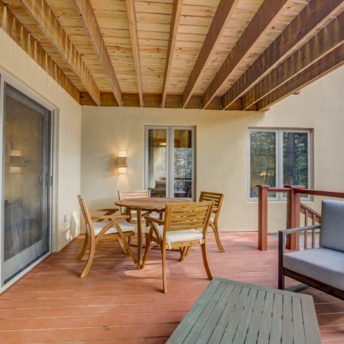 Covered outdoor patio with a wooden ceiling, dining table and chairs, a gray bench, and sliding glass doors.