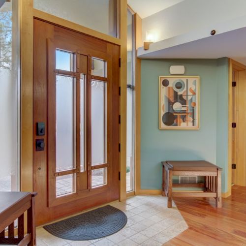 Bright entryway with wood double doors, tiled floor, small bench, and a framed abstract wall artwork.