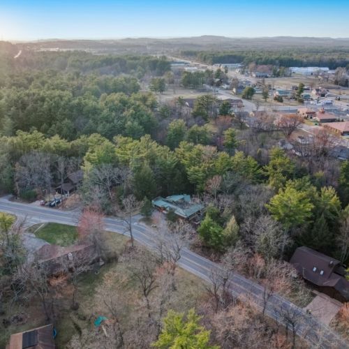 Aerial view of a small town with winding roads, scattered houses, and dense green forests under a bright sunrise sky.