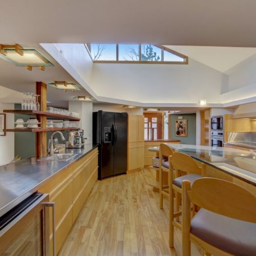 A bright modern kitchen with wood floors, long counters, an island-style workspace, stainless appliances, and large windows for light.