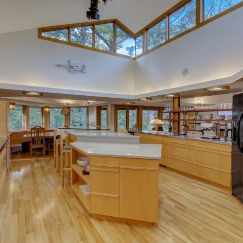 A bright modern kitchen with wood floors, large windows, and a central island, surrounded by stainless appliances.