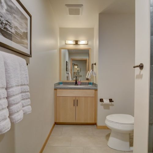 A modern bathroom with a toilet, vanity sink, towels, and a glass shower panel.