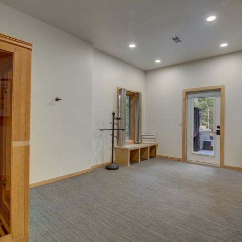 Bright room with carpet, a wooden sauna-style cabinet/door, coat rack, built-in bench, and windows with curtains.