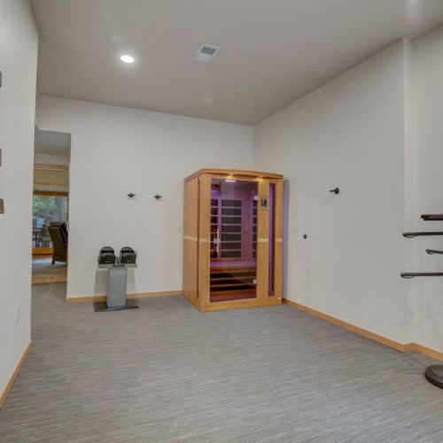A minimalist room with a wooden sauna door, shoe bench, and wall shelves beside a tall clothing rack stand.