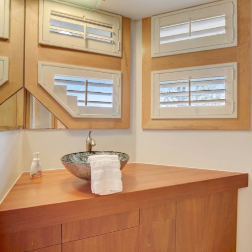 A wood bathroom vanity with a sink, soap, towel, faucet, and two small windows with blinds.