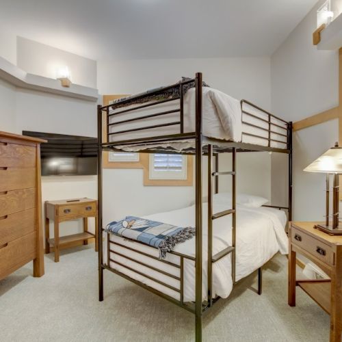 A tidy bedroom with a metal-framed bed, dresser, nightstand, lamp, and window shutters.