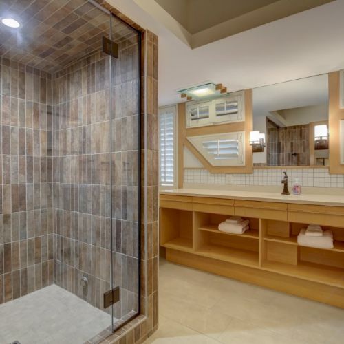 Modern bathroom with a glass shower, tiled walls, and a long wooden vanity with mirrors and neatly folded towels.