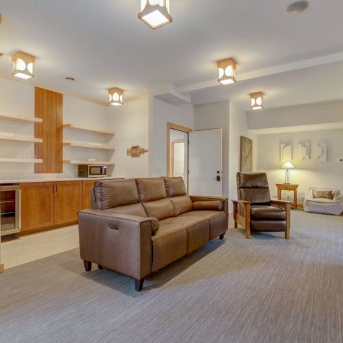 Modern living room with leather sofa, chairs, fireplace, and a small kitchen area with wood cabinetry and microwave.