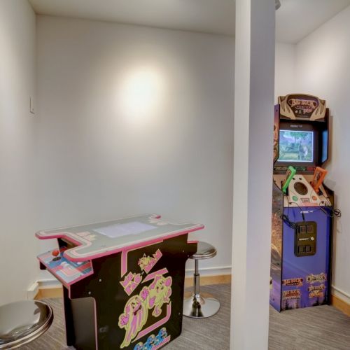An indoor arcade corner with a Big Buck Hunter game cabinet and a small arcade table against white walls.