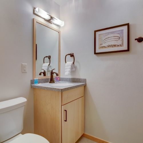 A small bathroom with a vanity sink, mirror, toilet, folded towels, and framed wall art.