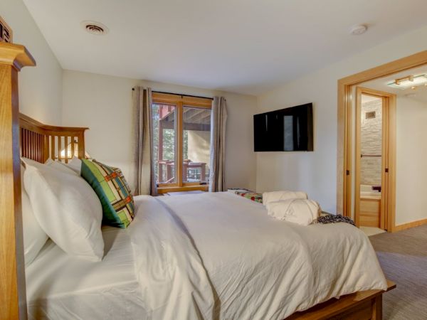 A bright bedroom with a large bed, patterned pillows, and a wall-mounted TV by a window.