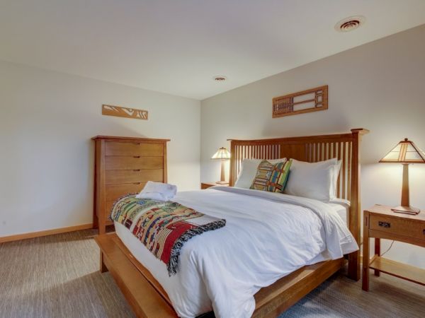 A bright bedroom with a wooden bed, white linens, bedside lamps, and matching dressers against cream walls.