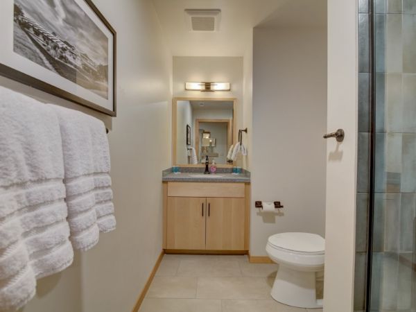 A modern bathroom showing folded towels, a vanity with blue cups, a toilet, and a glass-door shower with a grab bar.