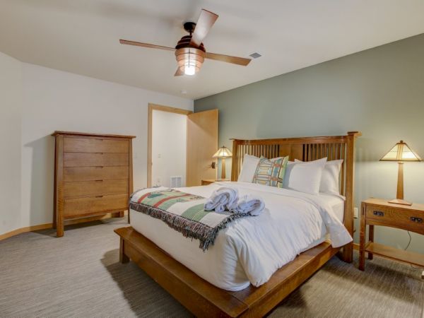 Clean bedroom with a wooden bed, dresser, two nightstands and lamps, and a ceiling fan overhead, with neatly folded linens.