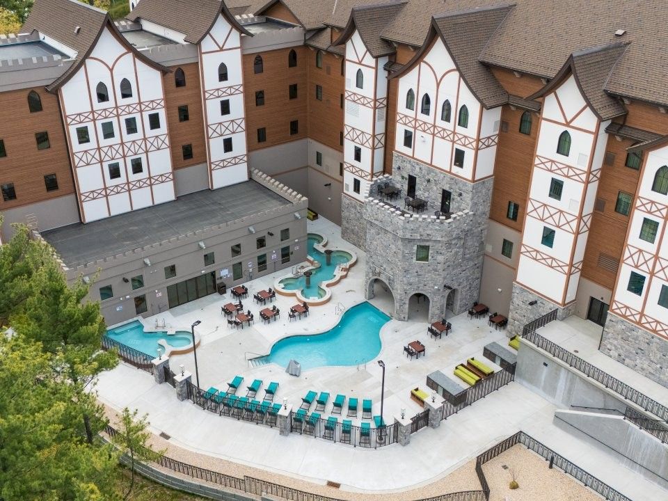 An aerial view of a Tudor-style courtyard hotel with a turquoise pool, stone archway, and tables set around the patio.