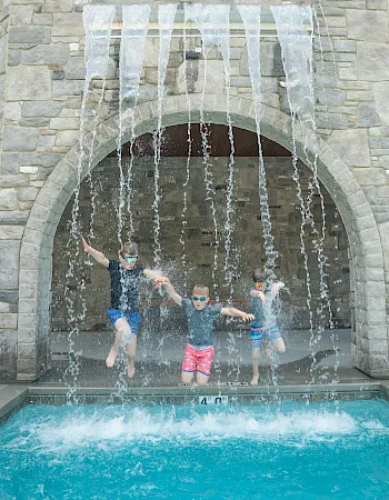 Kids splash through a waterfall into an outdoor pool.