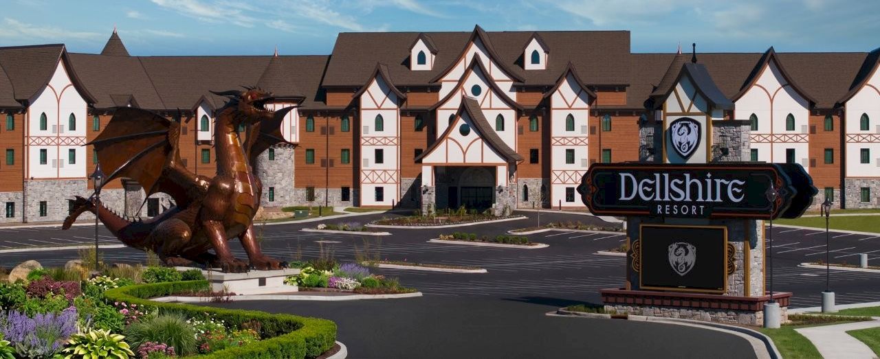A &ldquo;Delshire Resort&rdquo; sign and a large dragon statue sit in front of a fairytale-style hotel under a bright blue sky.